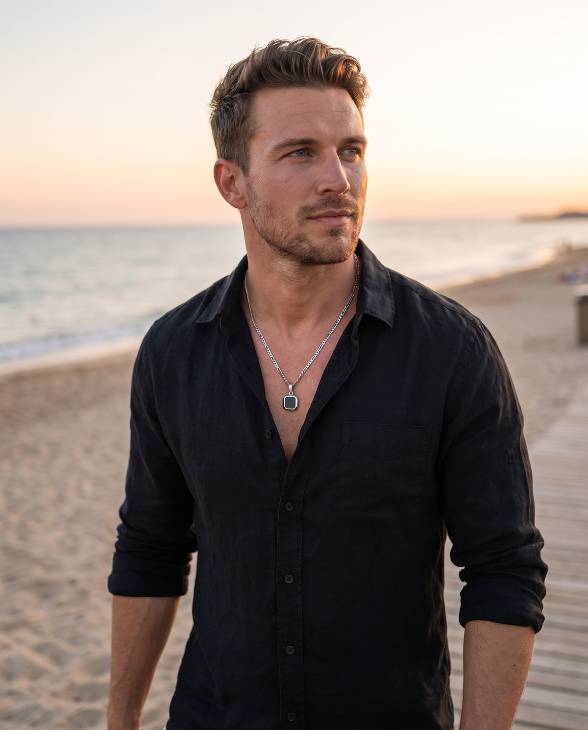 Man in a black linen shirt on a beach boardwalk wearing El Bloque silver black square pendant on a silver Figaro chain