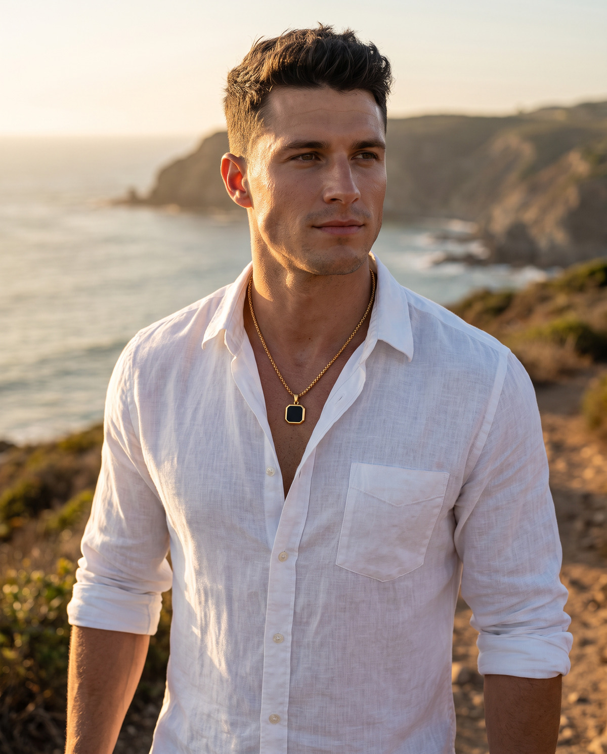 Man in a white linen shirt on a coastal trail wearing El Bloque gold black square pendant on a gold box chain