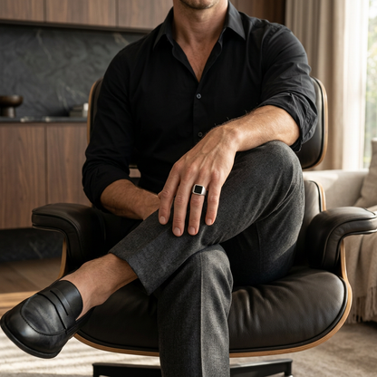 Man seated with crossed legs in a luxury home wearing the silver signet ring