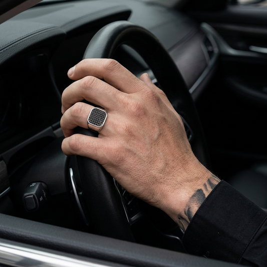 Masculine tattooed hand wearing the silver ring on a luxury black leather steering wheel