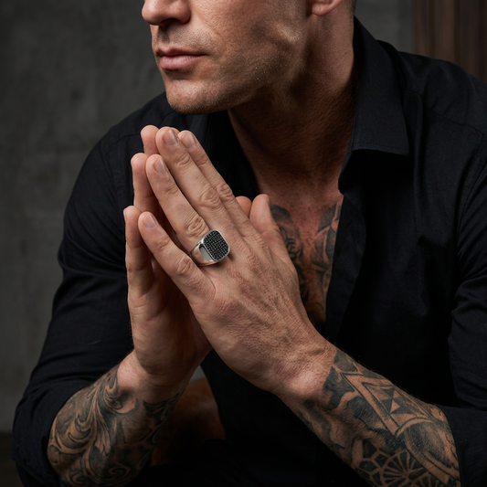 Tattooed seated male with hands together wearing the silver ring